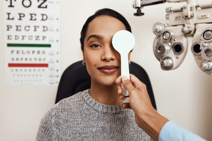 woman getting an eye exam, the optometrist is covering one of her eyes as part of a vision test