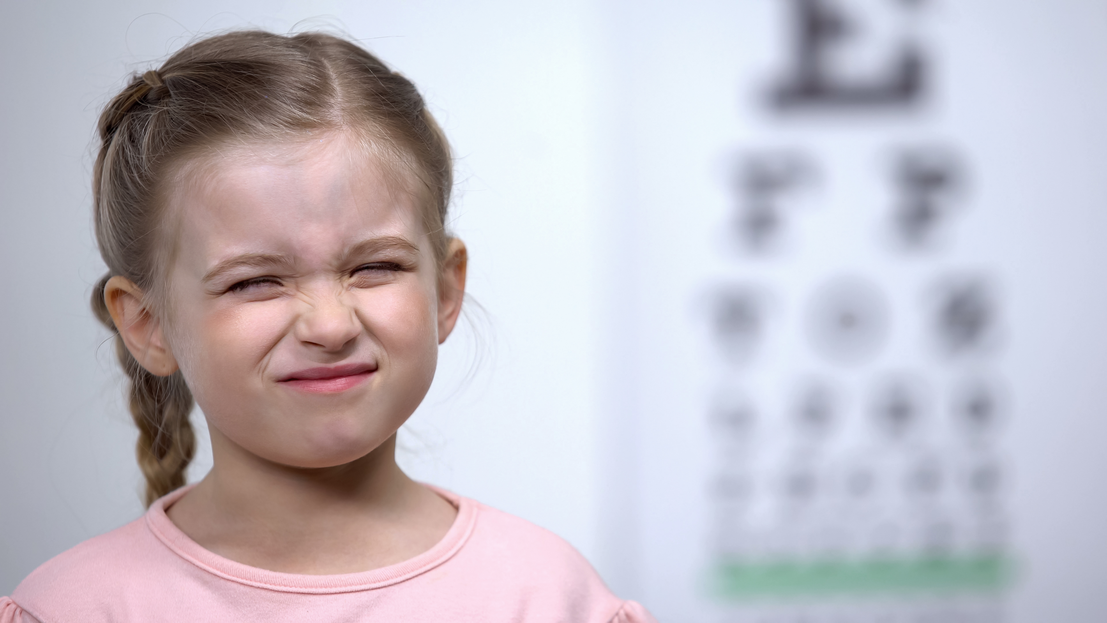 Small girl frowning, trying to see letters on an eye chart