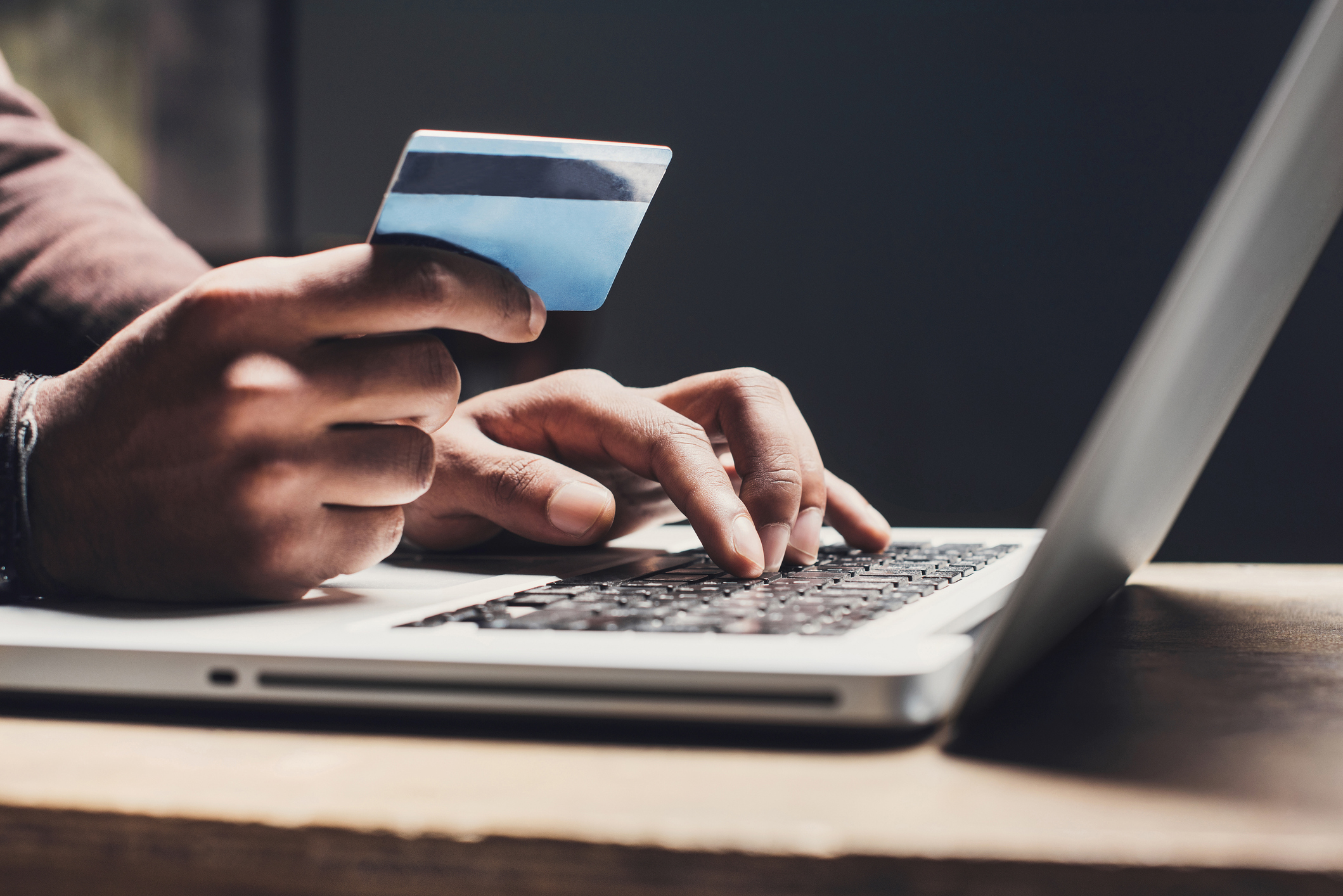 A person using a laptop, one hand is typing, the other hand holding a credit card, as if the person is going to place an online order