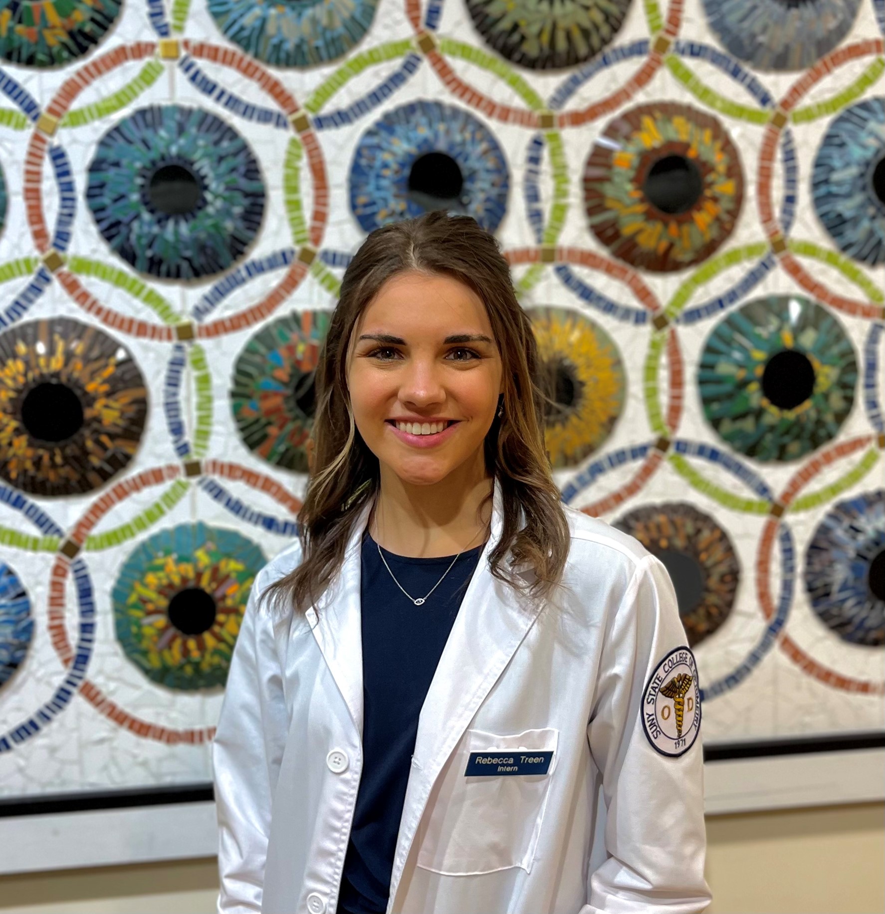 Optometry student standing in front of a background of different coloured eyes