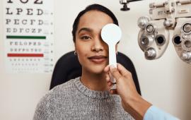 woman getting an eye exam, the optometrist is covering one of her eyes as part of a vision test