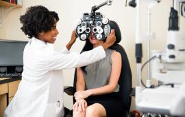 Optometrist using phoropter as she examines a patients eyes