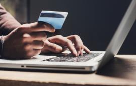 A person using a laptop, one hand is typing, the other hand holding a credit card, as if the person is going to place an online order