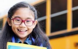 Girl with glasses in front of school bus