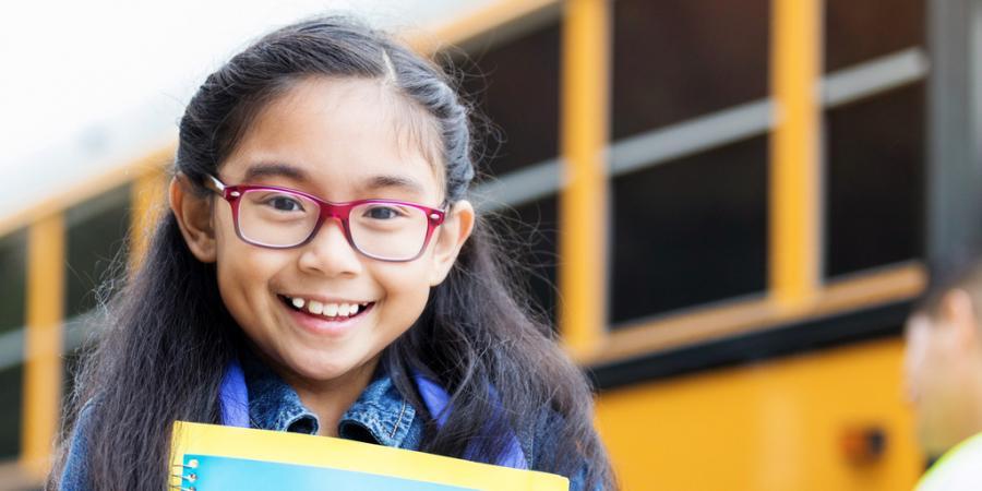 Girl with glasses in front of school bus