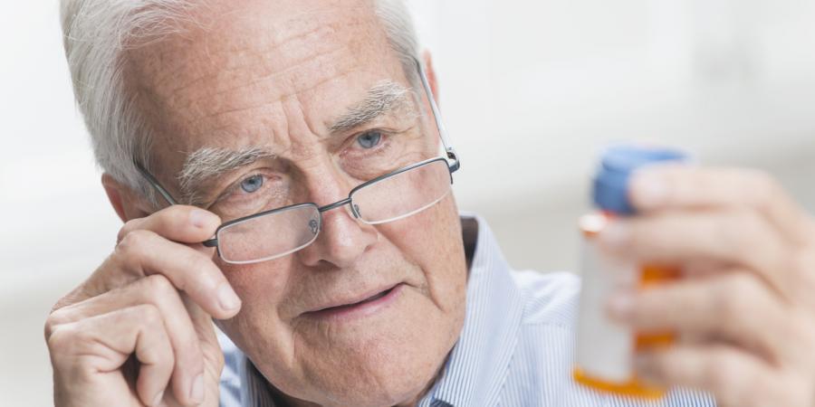 Male senior with glasses looking at a pill bottle