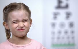 Small girl frowning, trying to see letters on an eye chart